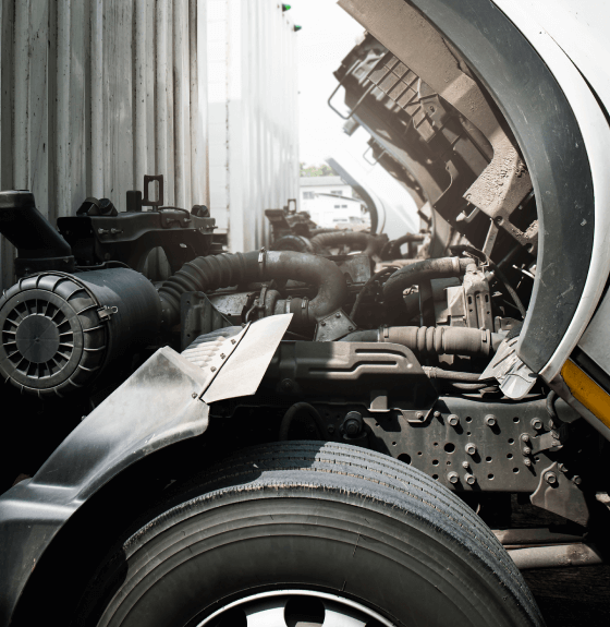 Camion avec son capot relevé, exposant le moteur et ses pièces mécaniques, notamment des tuyaux et composants thermiques.